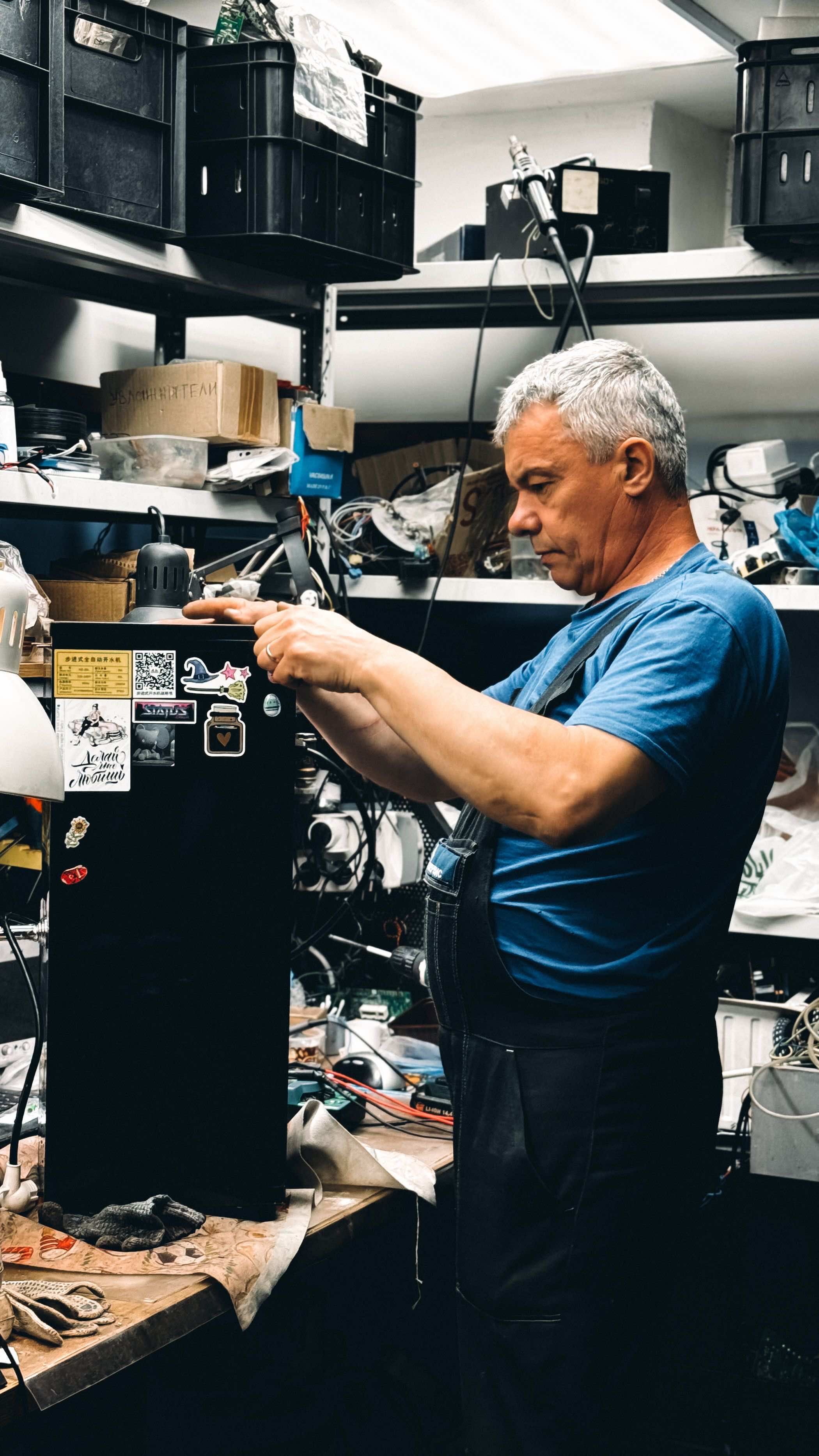 A senior technician repairing equipment at a workbench in a busy workshop